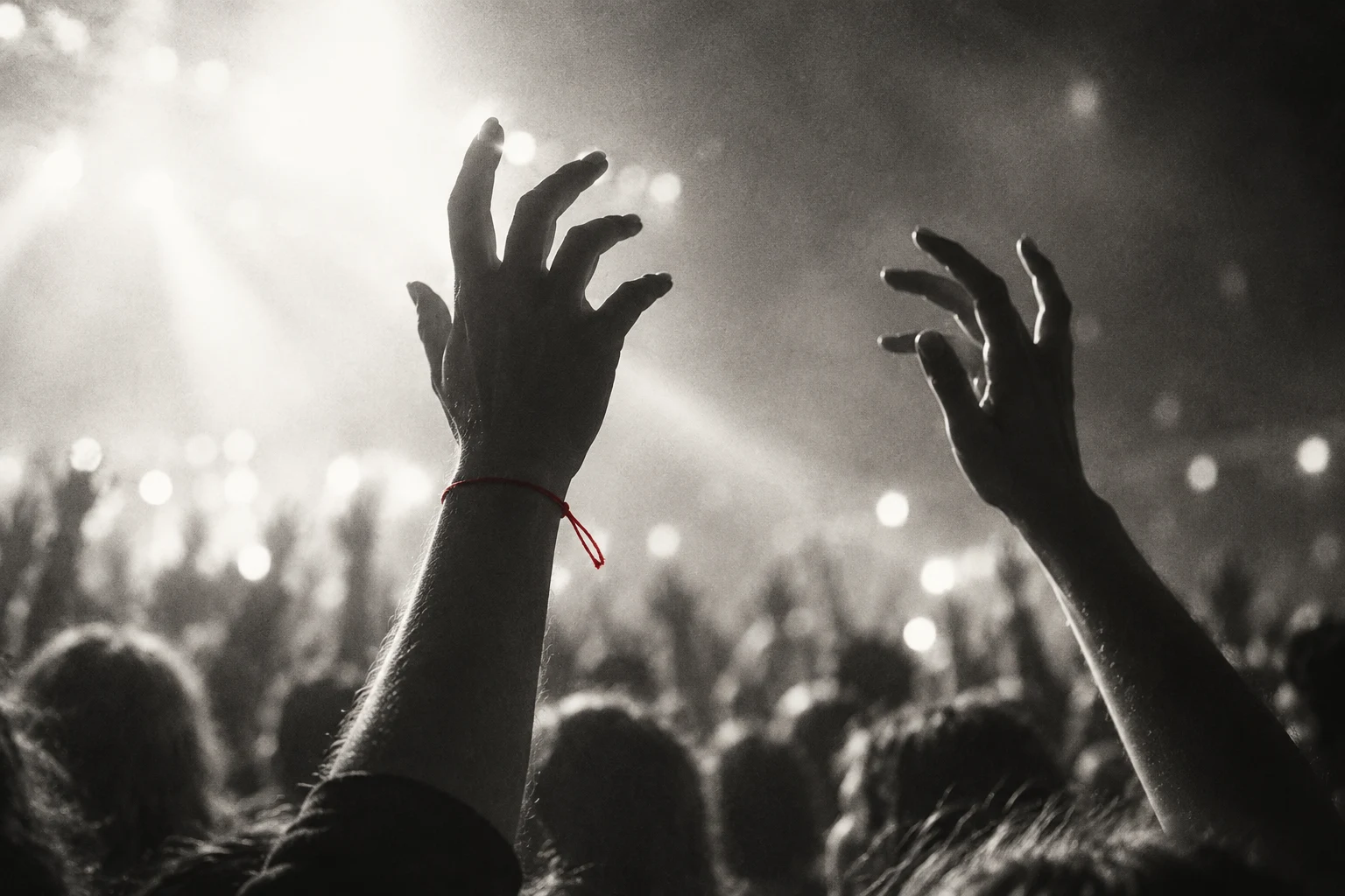 Hands raised into concert light, one wrist carrying a fine red thread.